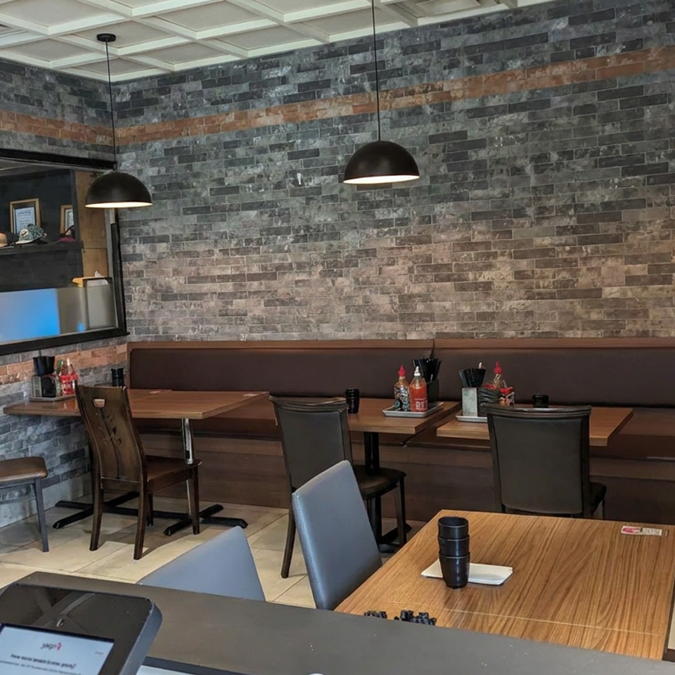 Modern restaurant dining area with wood tables, leather banquette seating, pendant lights, and a dark stone accent wall.
